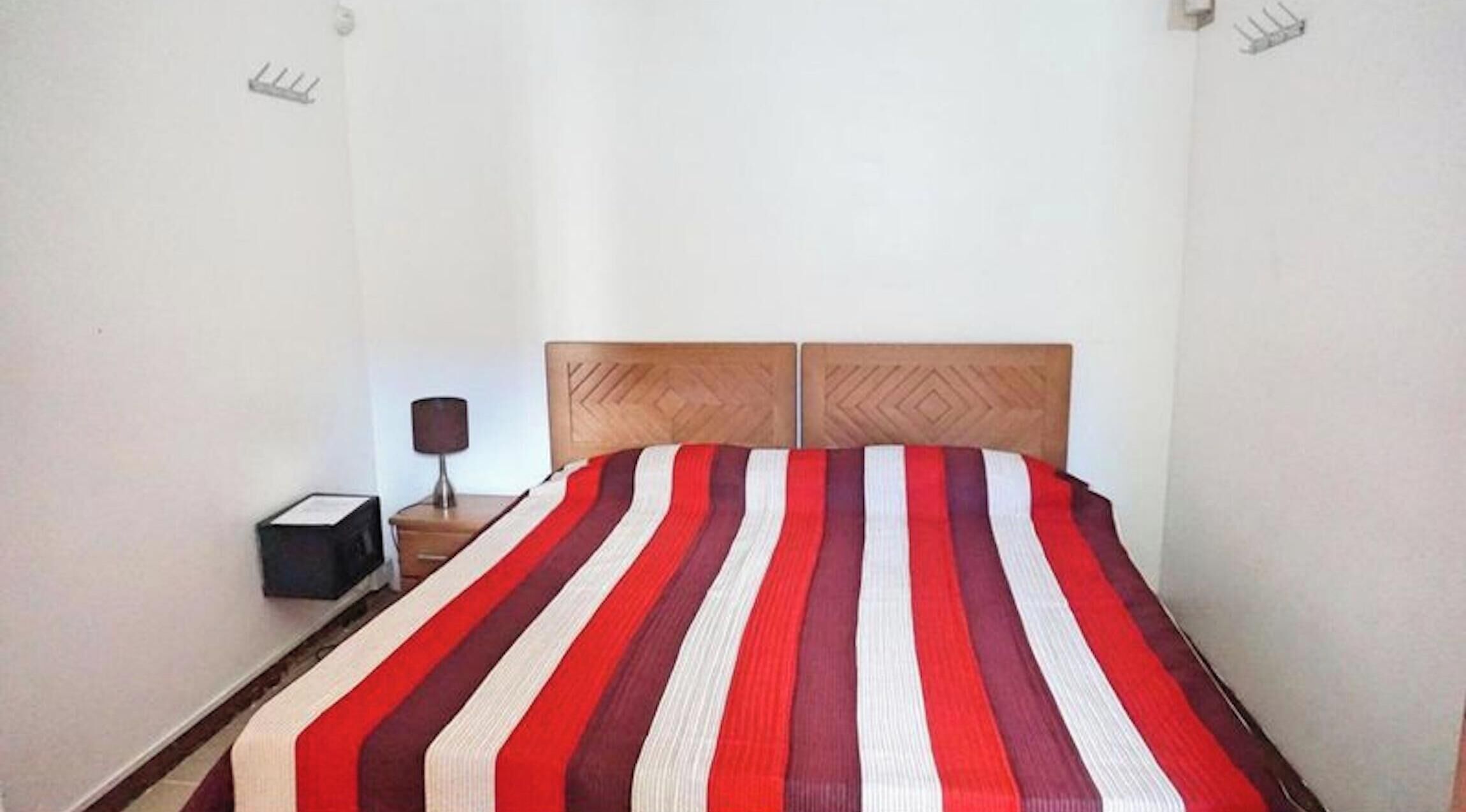 Una cama con una colcha a rayas, una mesita de noche con una lámpara y una caja pequeña.