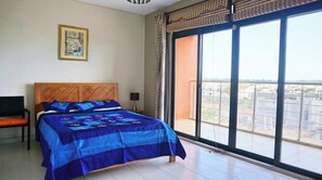 Ein Schlafzimmer mit einem großen Bett, einem Sessel, einem Nachttisch, einem Bild an der Wand und einem Balkon mit Aussicht.