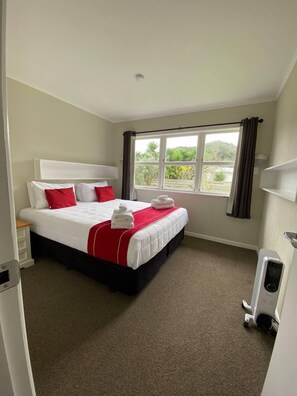 A hotel room with a bed, a window, a radiator, and a door.