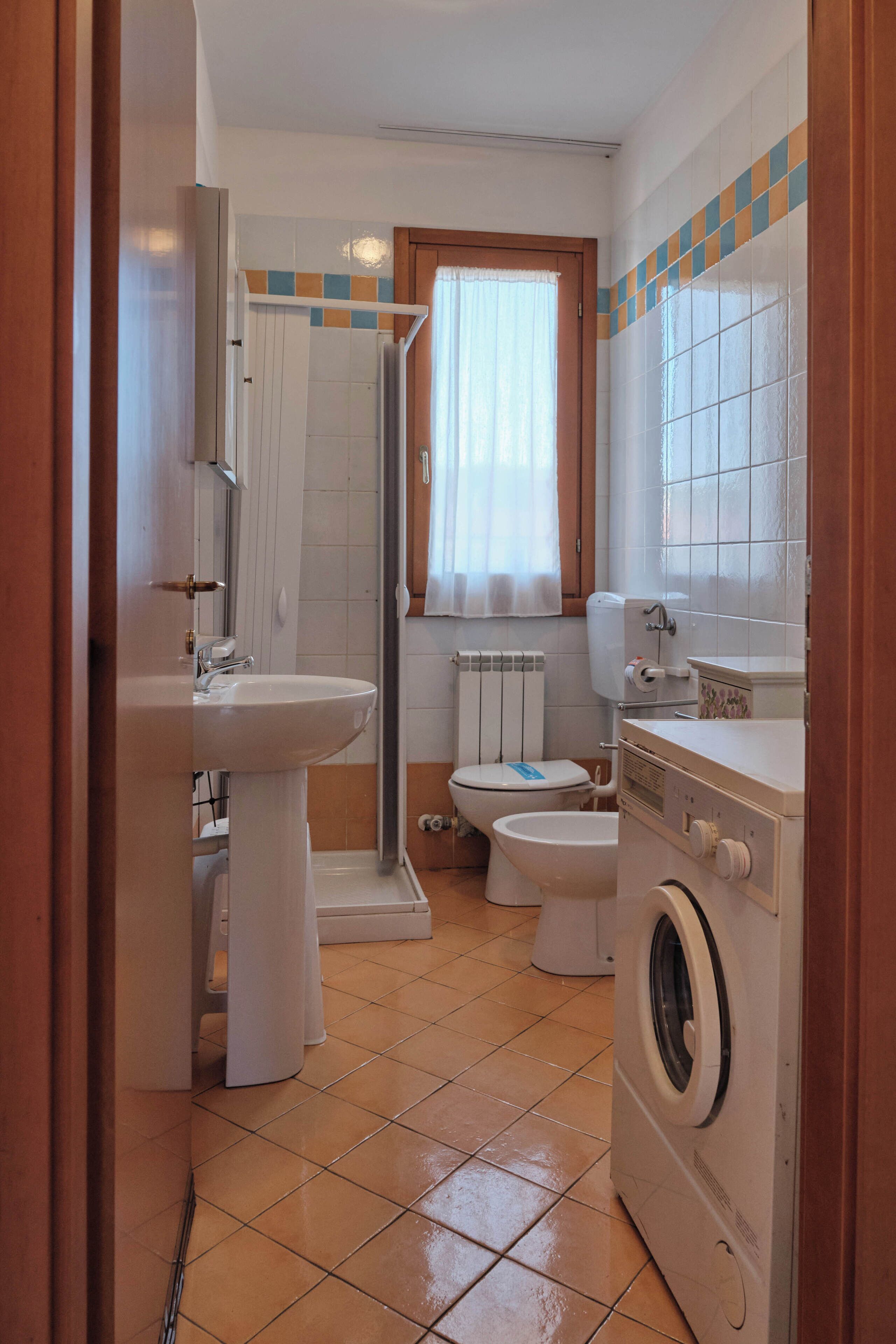 A compact bathroom with a sink, toilet, shower, and washing machine.