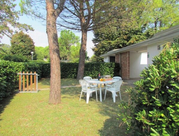 A patio with a table and chairs, surrounded by trees and a hedge.