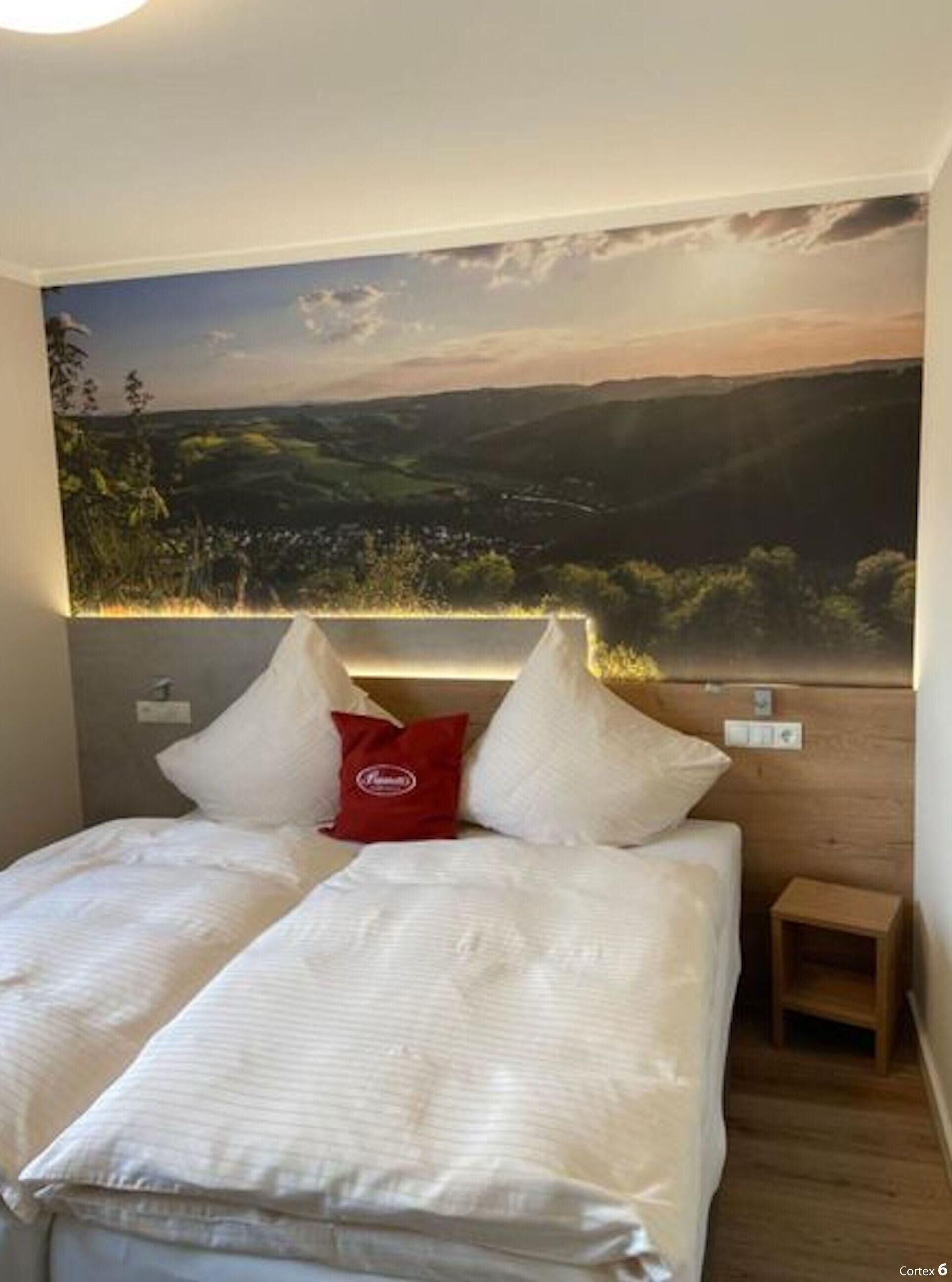 A bedroom with a bed, pillows, a nightstand, and a wall-mounted light.