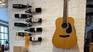 Een restaurantinterieur met een witte bakstenen muur, een gitaar en verschillende wijnflessen.