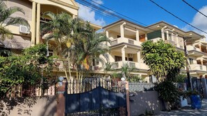 A residential building with multiple balconies, a gated entrance, and surrounding greenery.