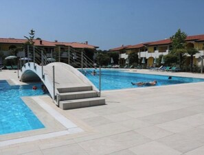 En swimmingpool med vandrutsjebane, liggestole og en bygning med rødt tag i baggrunden.