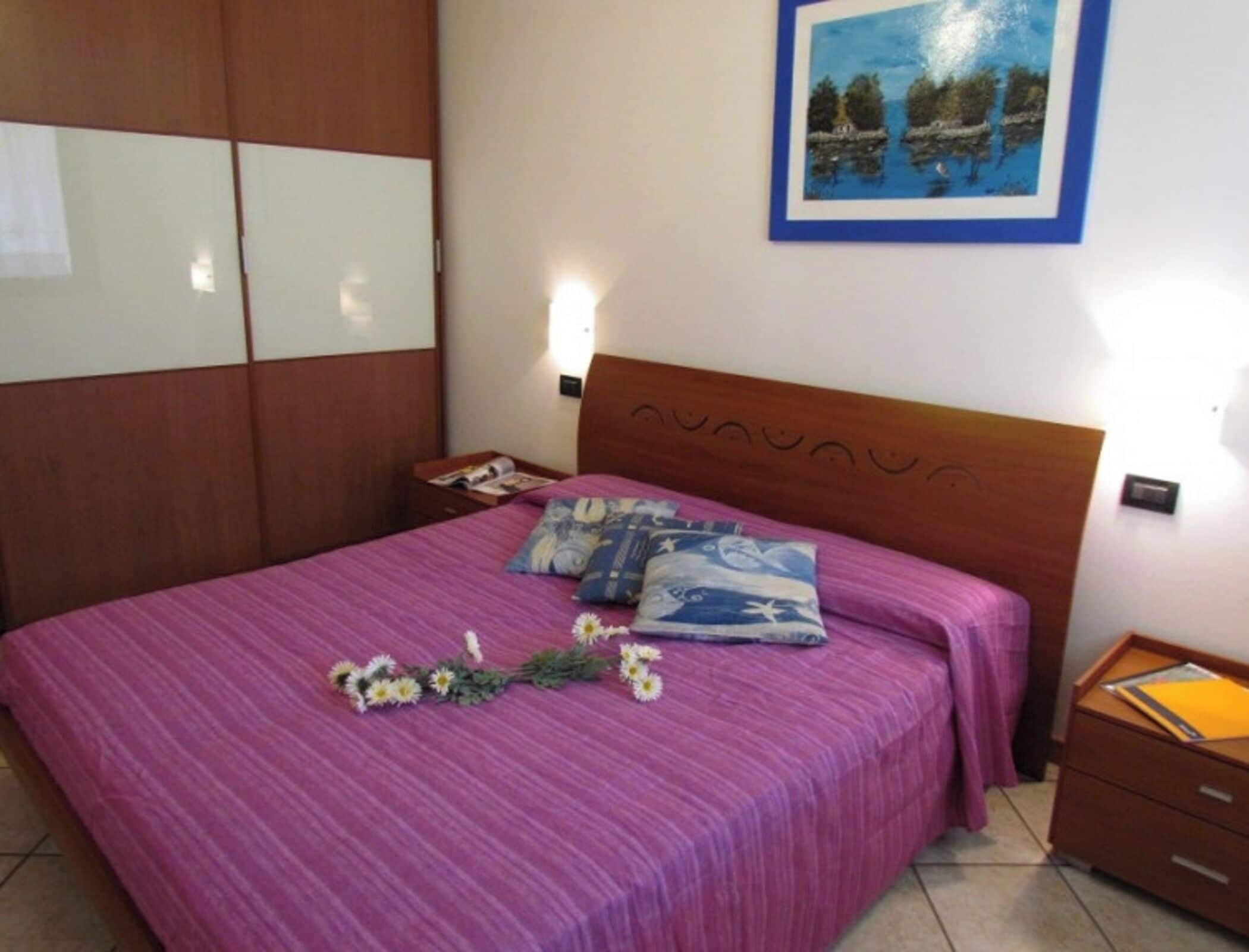 A bedroom with a wooden headboard, a purple bedspread, and a framed picture on the wall.