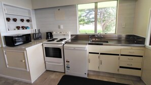 Cocina compacta con microondas, estufa, lavavajillas y ventana con vistas al verdor.