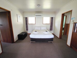 A hotel room with a bed, a suitcase, an air conditioning unit, and a window with curtains. - Te Ra Beach House (Paihia)