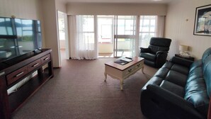 Una sala de estar con televisión de pantalla plana, un sofá de cuero, una mesa de centro y una silla.