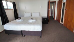Habitación de hotel con cama, mesita de noche, ventilador de techo y vista al exterior a través de una ventana.