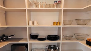 Una cocina con estantes blancos, distintos utensilios de cocina, un tostador y un lavabo.