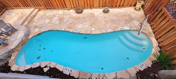 pool surrounded by lush greenery and a wooden fence.