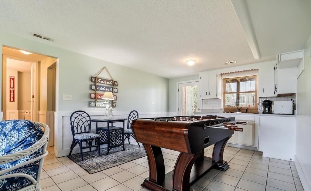 Una sala de estar acogedora con una mesa de fútbol, una mesa de comedor con sillas y una cocina con armarios y una ventana.