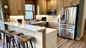 A modern kitchen with wooden cabinets, a stainless steel refrigerator, and a marble island with bar stools. - 2348 Red Hawk Townhomes 3 Bedroom Condo by RedAwning (Keystone)