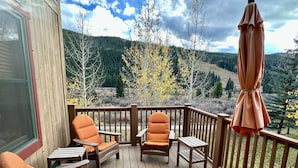 A wooden deck with outdoor furniture, including chairs and a table, overlooking a forested hillside. - 2348 Red Hawk Townhomes 3 Bedroom Condo by RedAwning (Keystone)