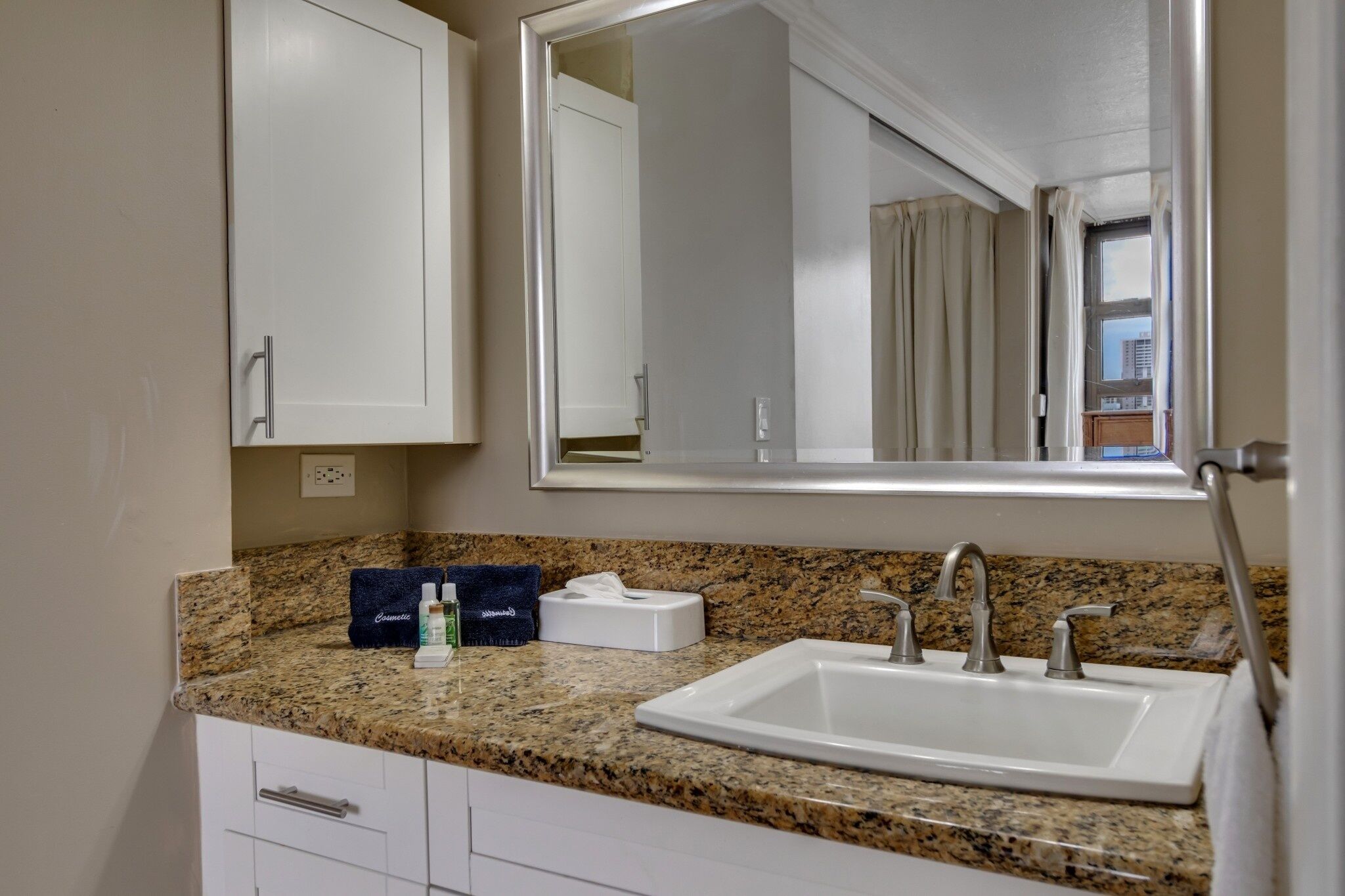 A bathroom with a granite countertop, a white sink, a mirror, and a towel rack.