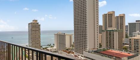 A high-rise hotel with multiple floors, a red-roofed tennis court, and a view of the ocean.