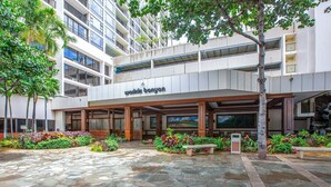 A modern building with a covered entrance, stone-paved courtyard, and lush greenery.