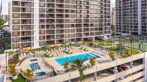A high-rise hotel with a rooftop pool, sun loungers, and a landscaped area.
