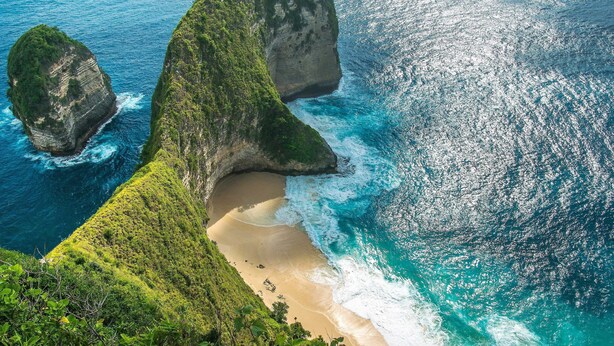 An aerial view of a coastal landscape with cliffs, a beach, and clear blue waters.