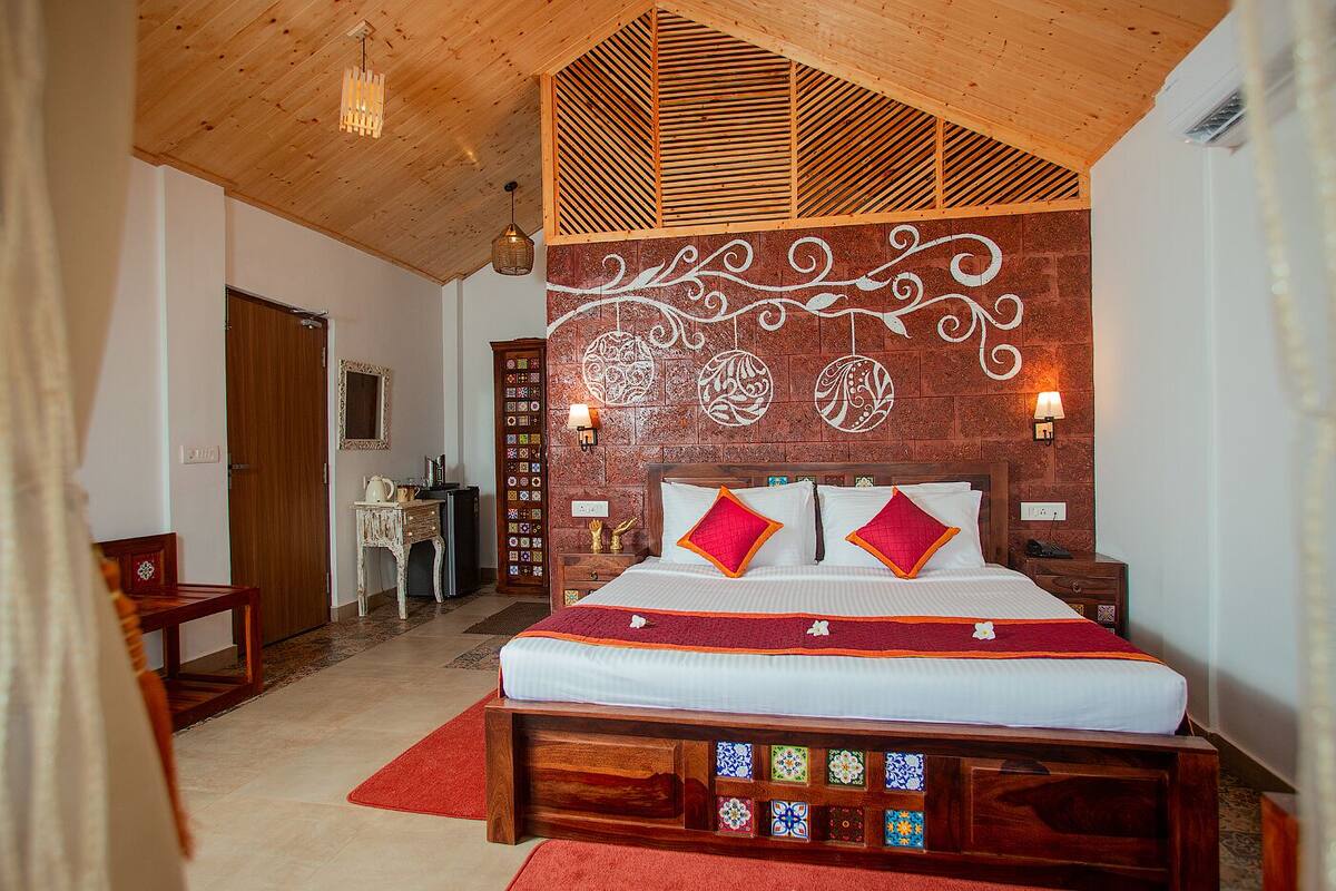 Un dormitorio con techo de madera, una cama con ropa de cama roja y blanca, una mesita de noche, un aparador y una pared con azulejos decorativos.