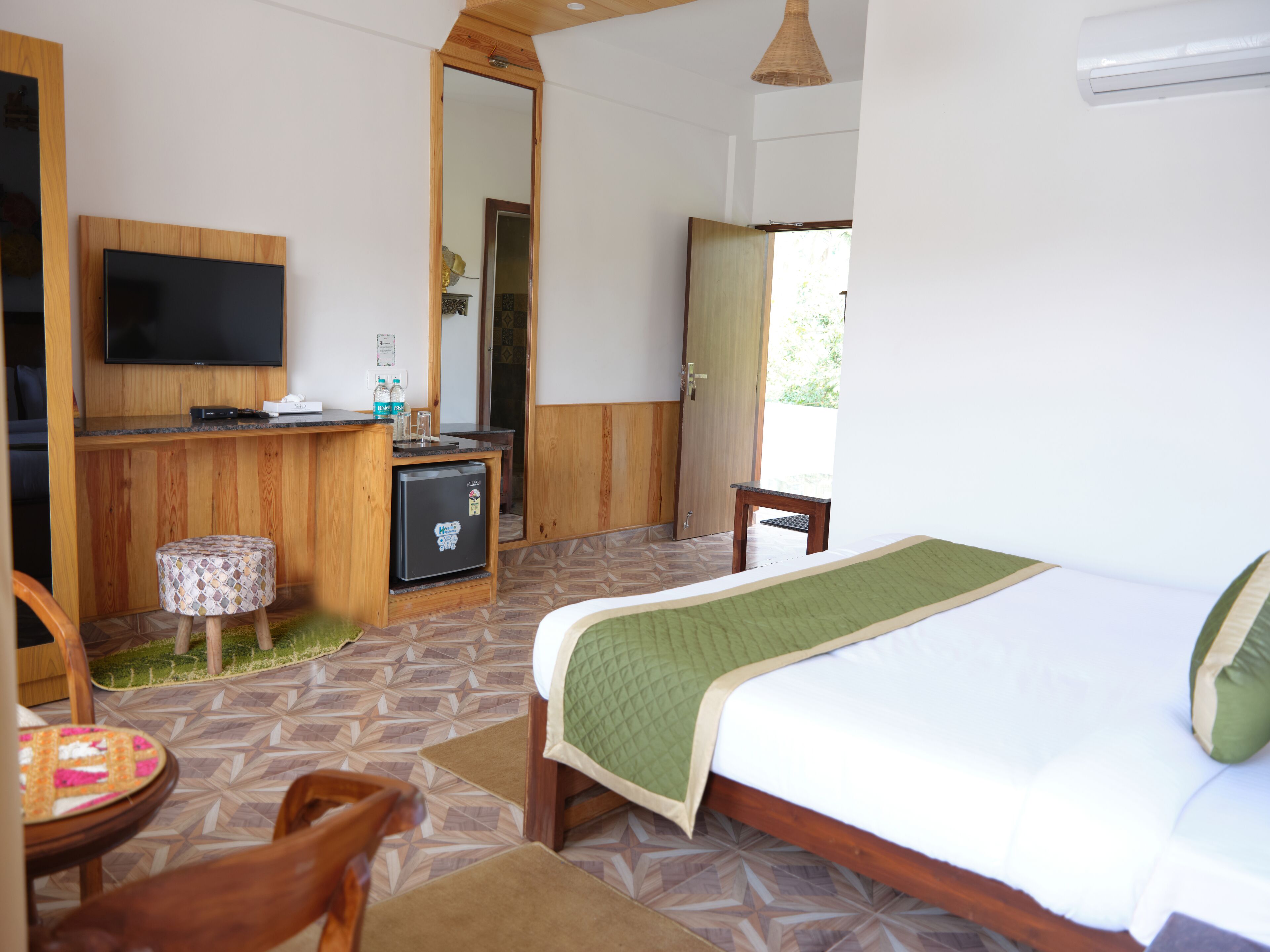 A hotel room with a bed, a small desk with a television, a refrigerator, and a chair.