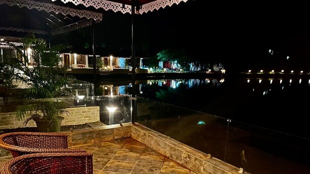 Un área de estar al aire libre con sillas de mimbre y piso de baldosas de piedra, con vista a una masa de agua tranquila que refleja luces.