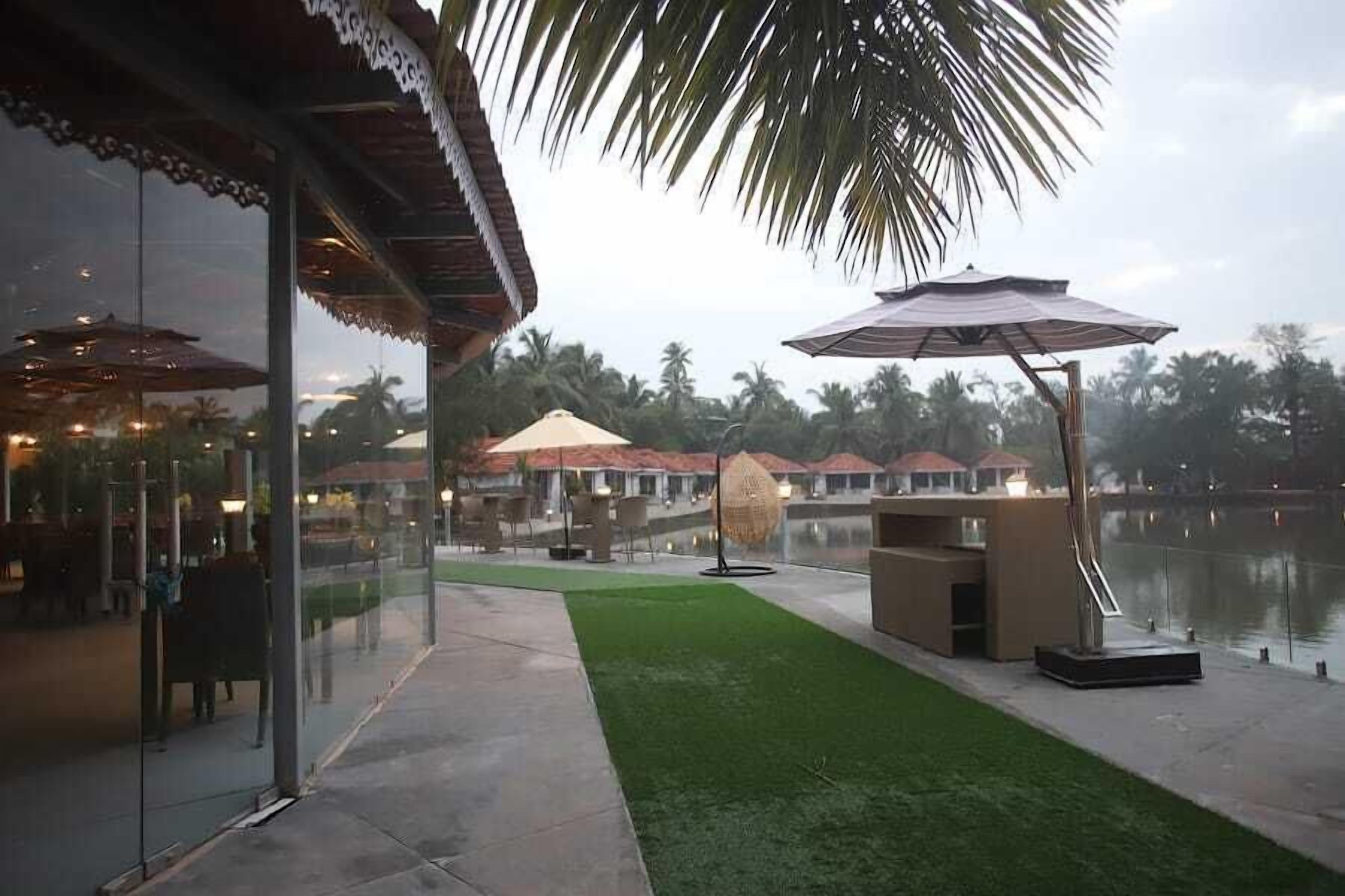 An outdoor area with a glass wall, a grassy patch, and a seating area with umbrellas.