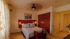 Een slaapkamer met een bed, nachtkastjes, een houten garderobe, een plafondventilator en een ingelijst schilderij aan de muur.