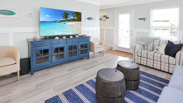 A living room with a television, a blue cabinet, a striped rug, and two wooden barrels. - The Ricks Carlton (Port St. Joe)