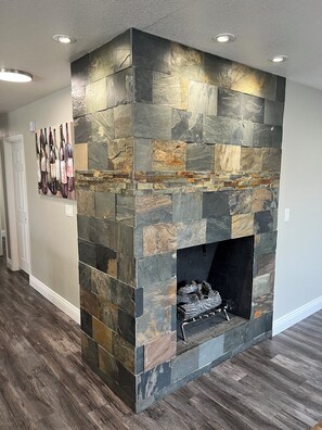 A stone fireplace with a log fire, a wall-mounted wine bottle art, and a wooden floor.