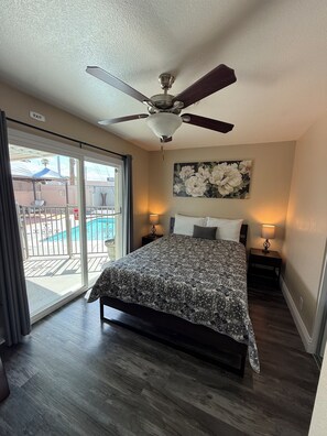 A bedroom with a bed, a ceiling fan, a painting, and a view of a swimming pool.