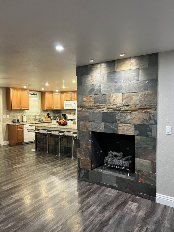 A modern kitchen with a stone fireplace, wooden cabinets, and a bar area.