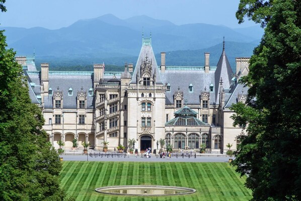 A grand historic building with a central courtyard, multiple towers, and a large lawn.