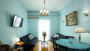 A living room with a sofa, a dining table, a TV mounted on the wall, and a chandelier. - Acropolis view vintage style apartment (Athens)