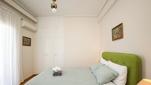 A bedroom with a green upholstered headboard, a bed with a green patterned bedspread, two pillows, and a pair of rolled towels on the bed. - Acropolis view vintage style apartment (Athens)