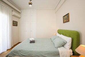 A bedroom with a green upholstered headboard, a bed with a green patterned bedspread, two pillows, and a pair of rolled towels on the bed. - Acropolis view vintage style apartment (Athens)