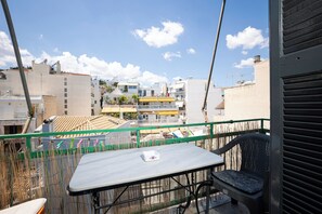 A balcony with a table and chair, overlooking a cityscape with buildings and a clear sky.