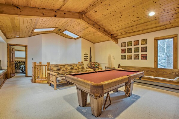 A wooden ceiling with skylights, a pool table, a sofa, and a wall with framed pictures.