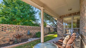 A patio with a glass table and metal chairs, a brick wall, and a covered area with a window.
