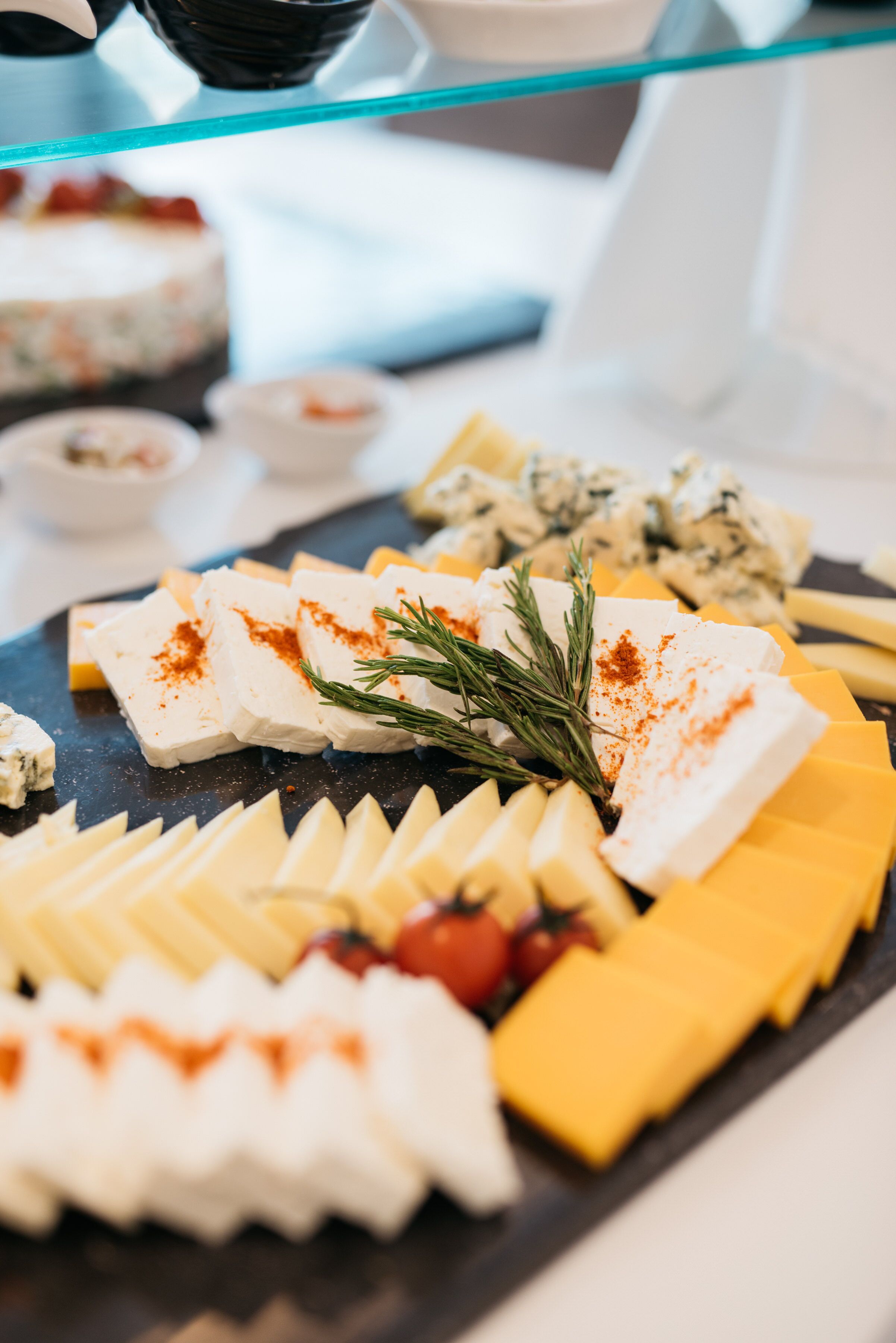 A cheese platter with various cheeses, garnishes, and a sprig of rosemary.