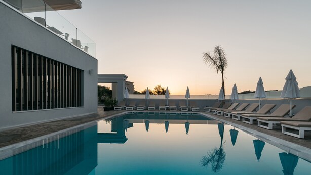 A modern pool area with lounge chairs and umbrellas, reflecting the sunset. - Tesoro Hotel Zakynthos (Zakynthos)