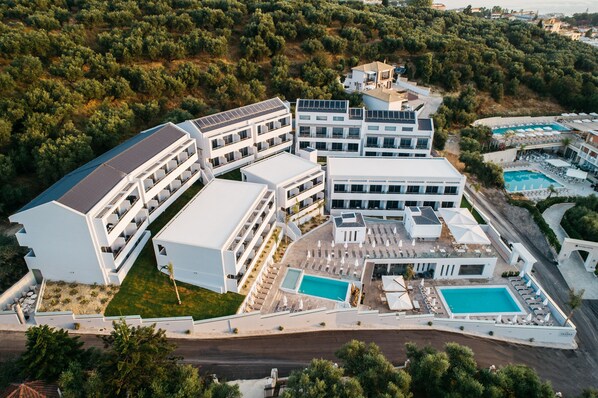 Vista aérea de un hotel moderno con varias construcciones, una piscina y zonas ajardinadas.