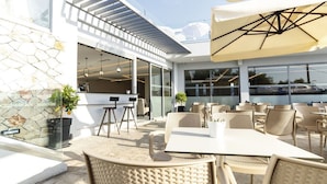 An outdoor patio area with wicker furniture, a bar area, and large windows offering views of the surroundings. - Tesoro Hotel Zakynthos (Zakynthos)