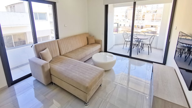 Een moderne woonkamer met een beige bank, een witte salontafel en een balkon met buitenmeubilair.