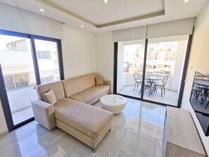 Uma sala de estar moderna com um sofá bege, uma mesa de centro branca e uma varanda com mobiliário de exterior.