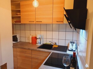 A compact kitchen with wooden cabinets, a microwave, a coffee maker, a toaster, and a wine glass. - Schnitterhaus Milena on Lake Flee - Milena Vacation Home on Lake Flee (Göhren-Lebbin)