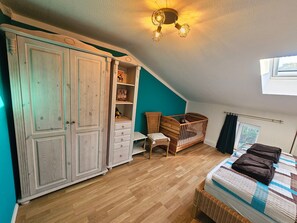 A room with a large wardrobe, a crib, a bed with towels, a small table, and a wall-mounted light fixture. - Schnitterhaus Milena on Lake Flee - Milena Vacation Home on Lake Flee (Göhren-Lebbin)