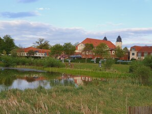 A building with a red roof and a tower, surrounded by greenery and a pond.