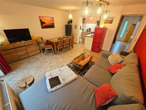 A living room with a sofa, a coffee table, a TV, and a dining area with chairs and a table. - Schnitterhaus Milena on Lake Flee - Milena Vacation Home on Lake Flee (Göhren-Lebbin)